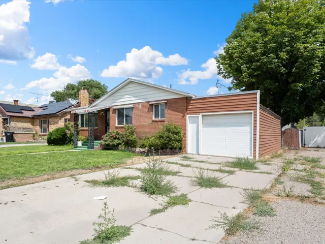 Brick exterior, attached garage with roll-up door, covered front porch, mature trees, and concrete driveway