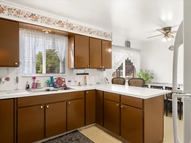 Kitchen featuring brown cabinetry, white countertops, dual basin sink, and a ceiling fan