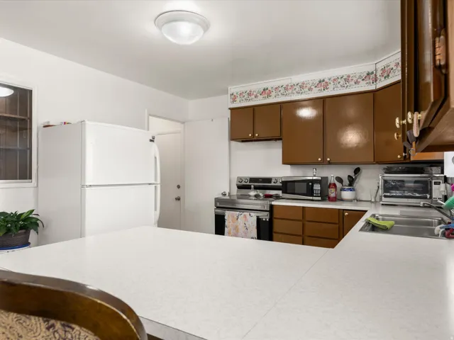 Kitchen featuring white countertops, brown cabinetry with gold-tone hardware, and a stainless steel range