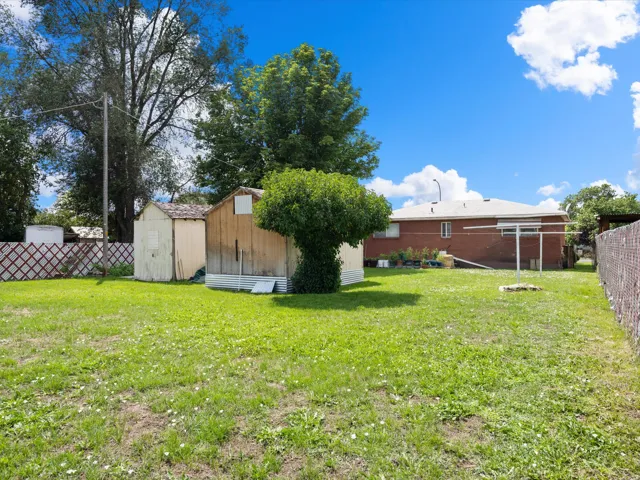 Spacious backyard featuring a grass lawn, two storage sheds, and mature perimeter trees