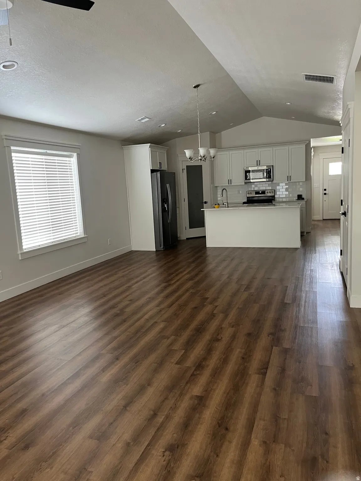 Vaulted ceilings with recessed lighting, wood-finish flooring throughout, kitchen with white cabinetry and stainless steel appliances, and a kitchen island