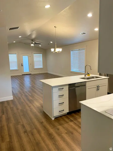 Vaulted ceiling, recessed lighting, wood-finish flooring, white kitchen island with integrated sink, and stainless steel dishwasher