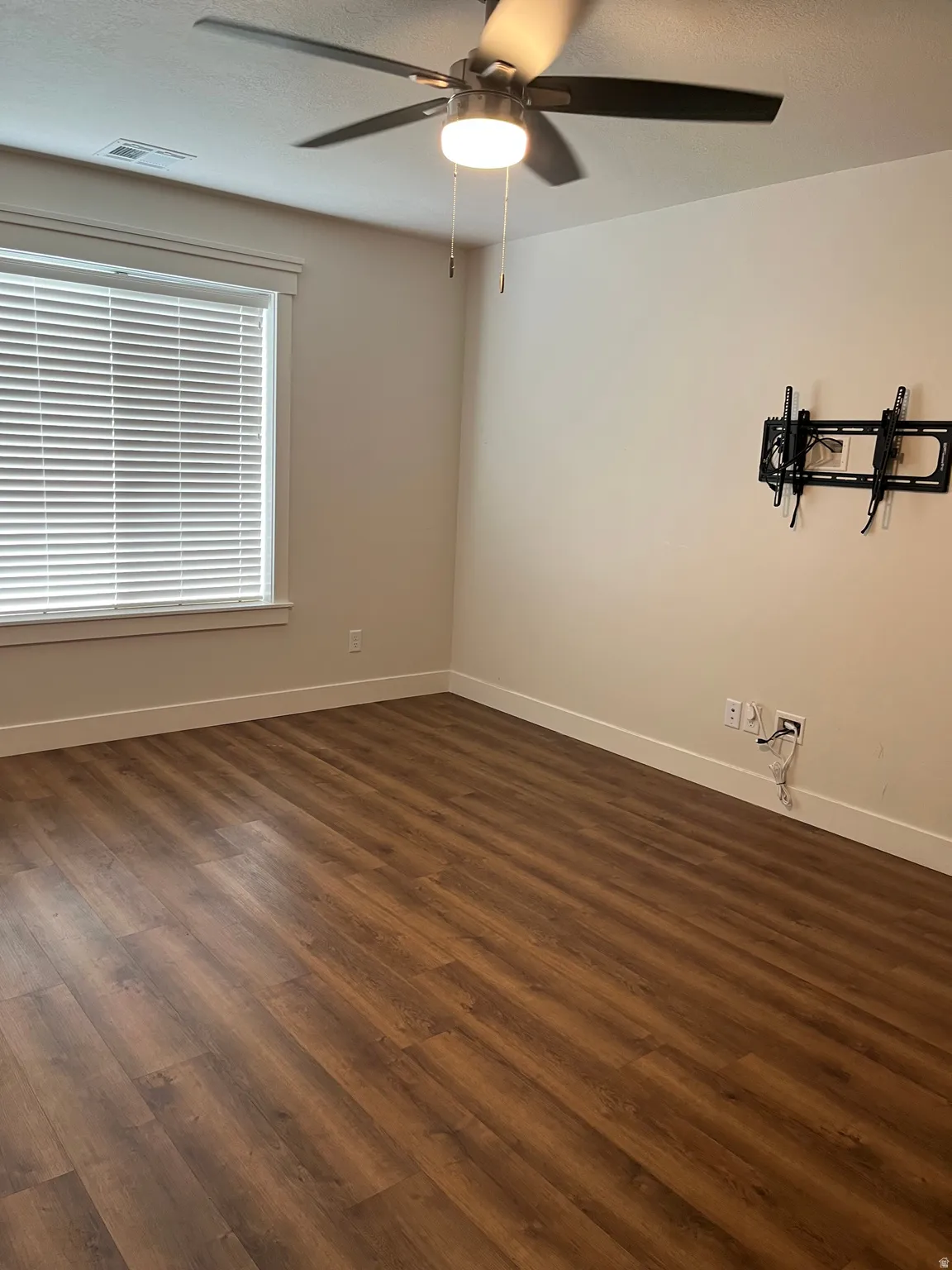 Wood-finish flooring, ceiling fan with integrated lighting, window with blinds, and white trim