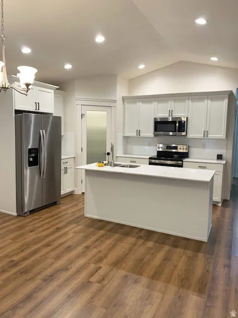 Kitchen featuring wood-finish flooring, white cabinetry, a central island with an undermount sink, stainless steel appliances, and recessed lighting