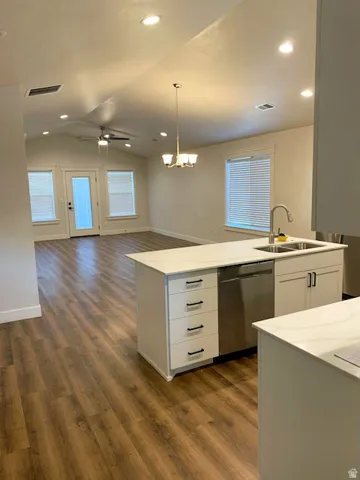 Vaulted ceiling, recessed lighting, wood-finish flooring, white kitchen island with integrated sink, and stainless steel dishwasher
