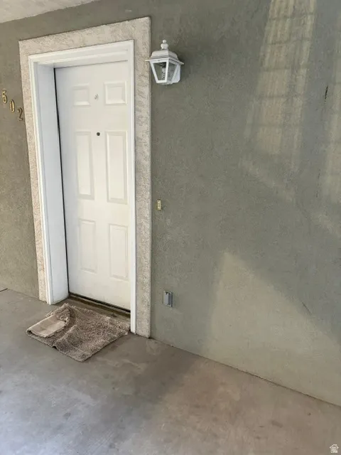 Textured stucco exterior with a paneled entry door, decorative door trim, and an exterior wall lantern