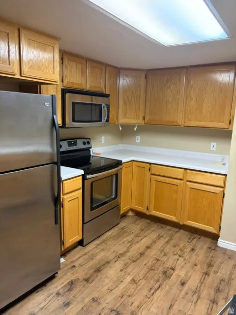 Kitchen featuring stainless steel appliances, wood-finish flooring, light-toned countertops, and wood cabinetry