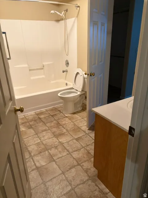 Bathroom featuring a shower/tub combination, toilet, light wood-finish vanity with an integrated sink, and square tile flooring