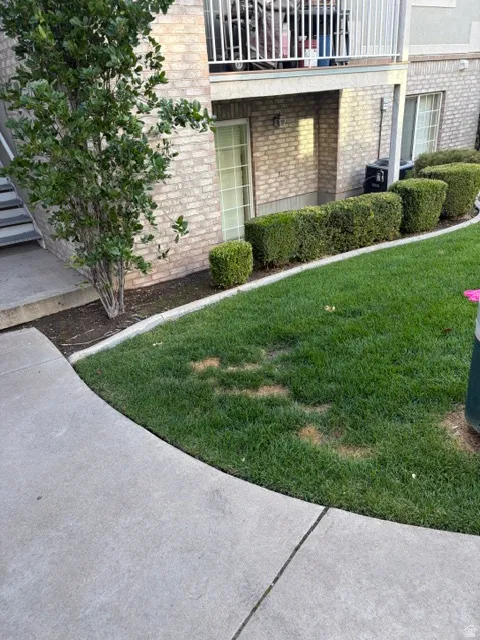 Brick exterior, concrete pathway, manicured lawn, established shrubbery, second-story balcony with white railing