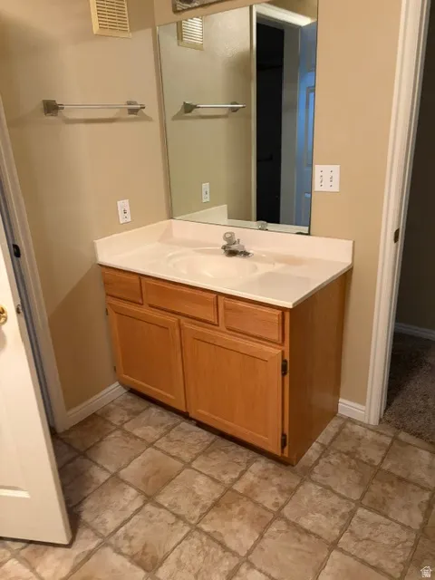 Vanity with integrated sink, light wood-finish cabinetry, and neutral countertop