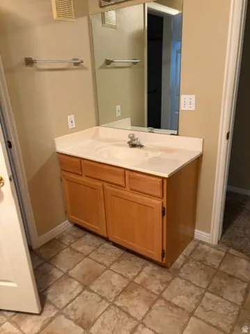 Vanity with integrated sink, light wood-finish cabinetry, and neutral countertop