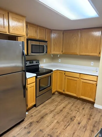 Kitchen featuring stainless steel appliances, wood-finish flooring, light-toned countertops, and wood cabinetry