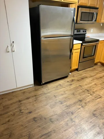 Stainless steel appliances, wood-finish flooring, white countertops, and light wood cabinetry