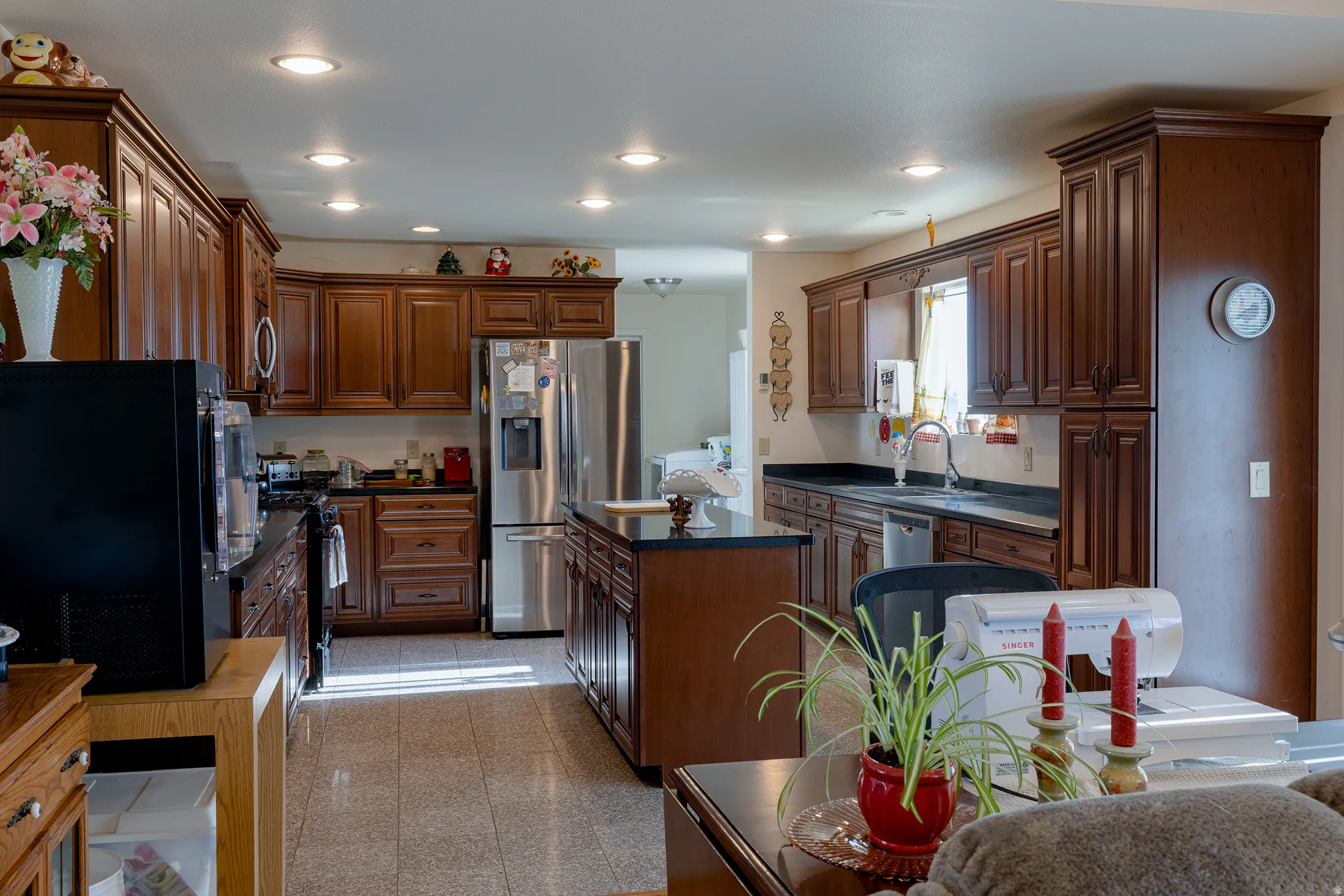 Kitchen featuring extensive wood cabinetry, recessed lighting, central island with dark countertop, stainless steel appliances, and tiled flooring