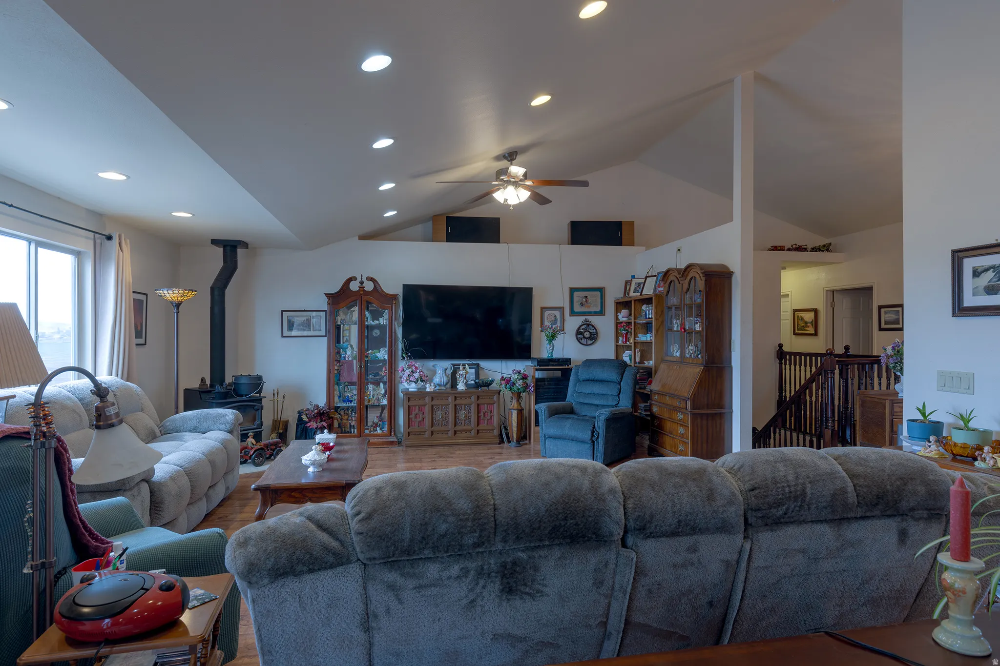 Vaulted ceilings with recessed lighting, wood-finish flooring, and a built-in wood stove