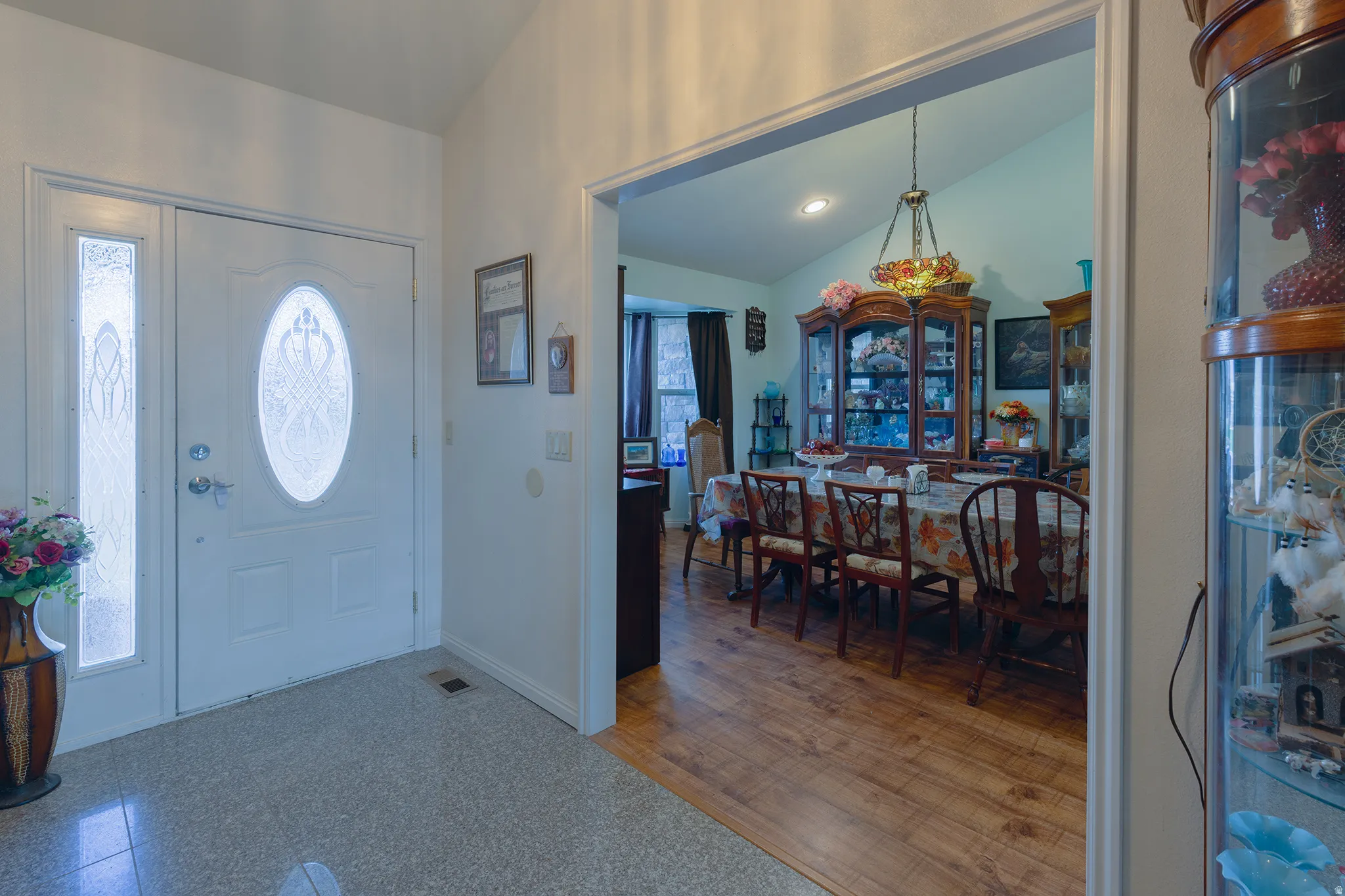Entryway with a decorative glass front door and side panel, leading to a dining area with wood-finish flooring and a vaulted ceiling