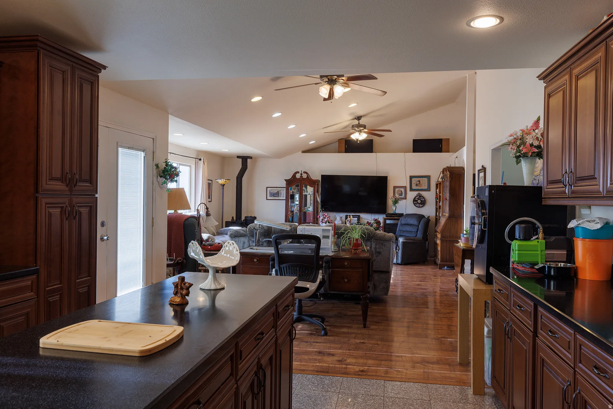 Open-concept living area featuring vaulted ceilings, wood-finish flooring, recessed lighting, and a wood-burning stove