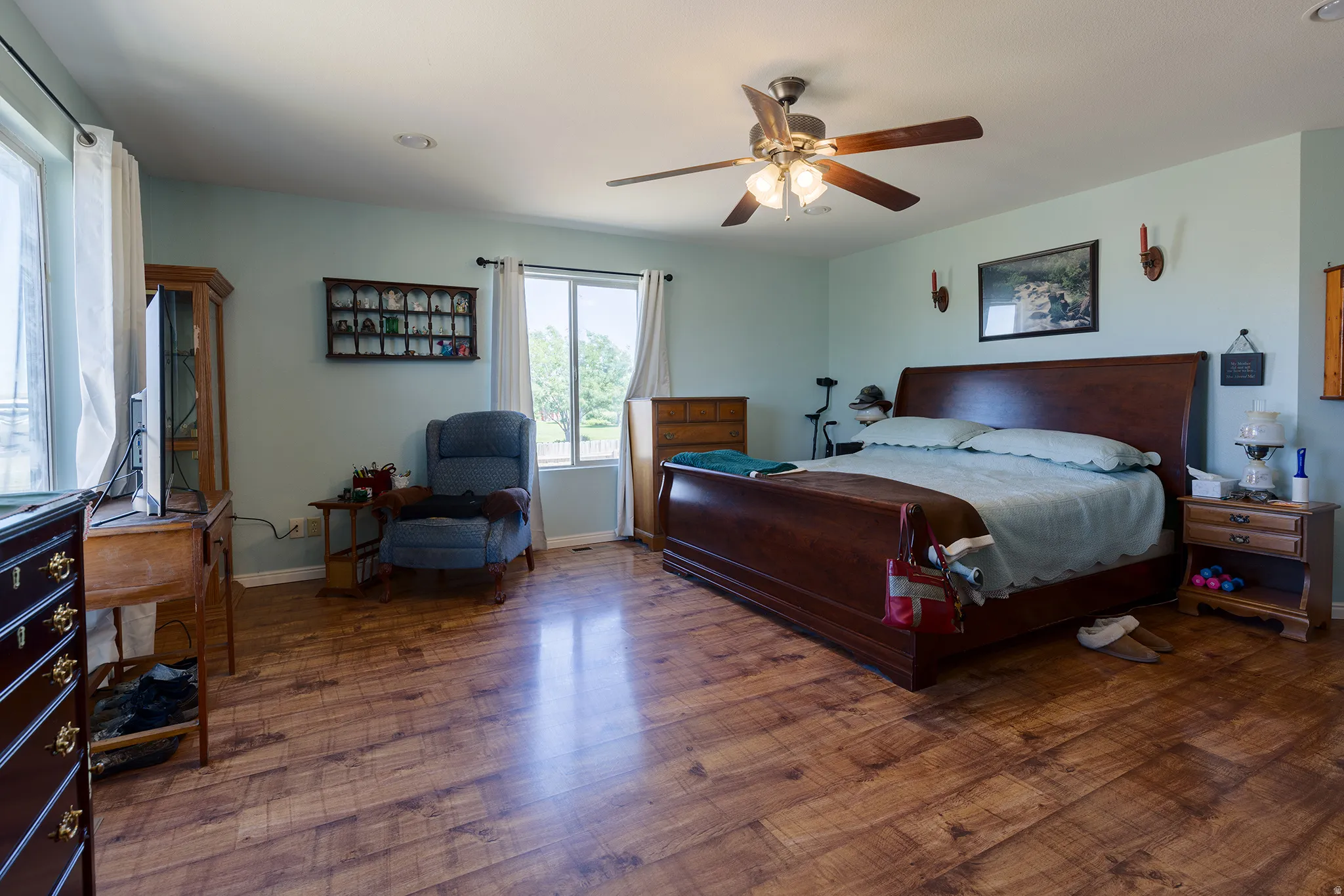 Wood-finish flooring, multiple windows, ceiling fan with integrated lighting, and light-colored wall paint