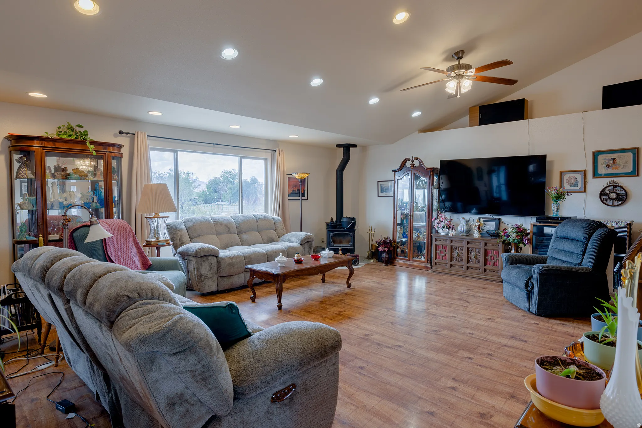Expansive room with wood-finish flooring, recessed lighting, a ceiling fan, and a wood-burning stove