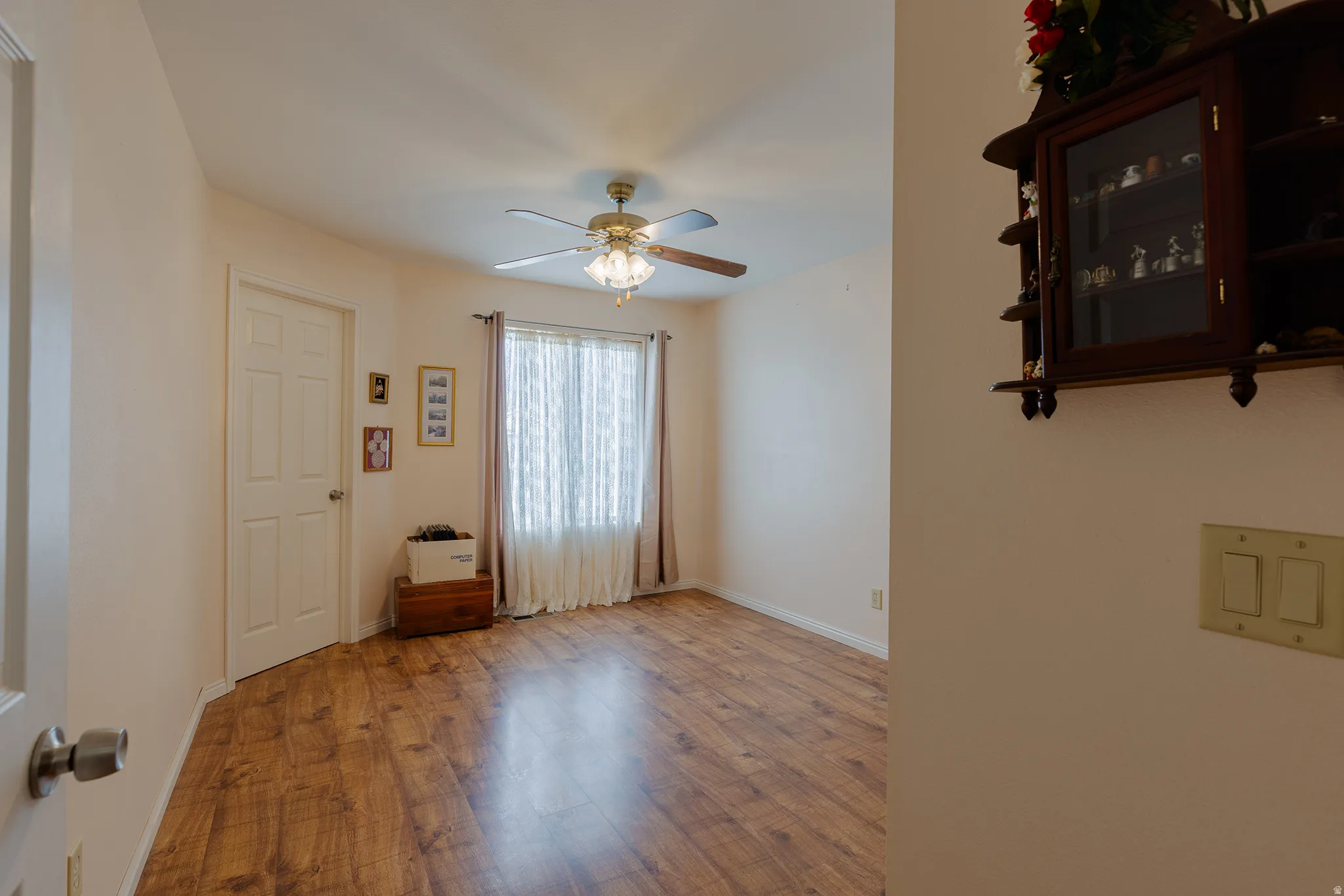 Wood-finish flooring with a ceiling fan light fixture and a window with vertical blinds