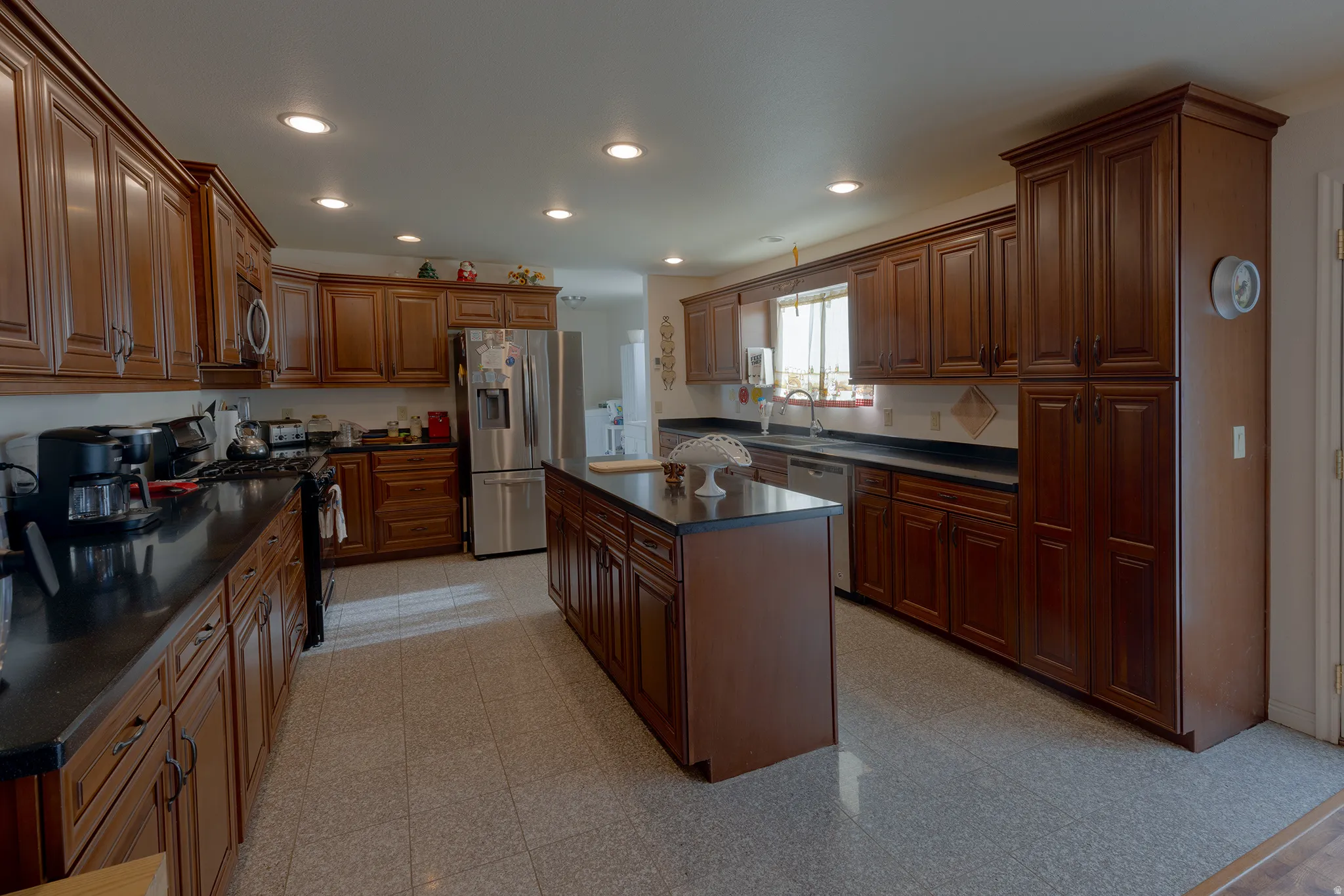 Kitchen with extensive wood-finish cabinetry, black countertops, a stainless steel refrigerator, and a central island with storage
