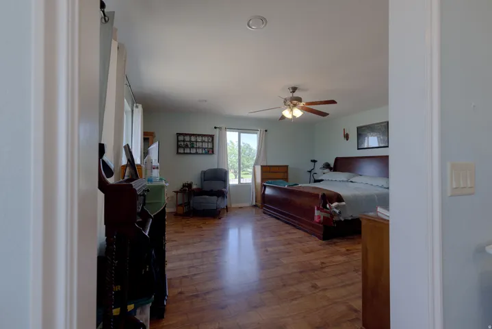 Expansive room featuring wood-finish flooring, light blue wall tones, multiple windows, and a ceiling fan with integrated lighting