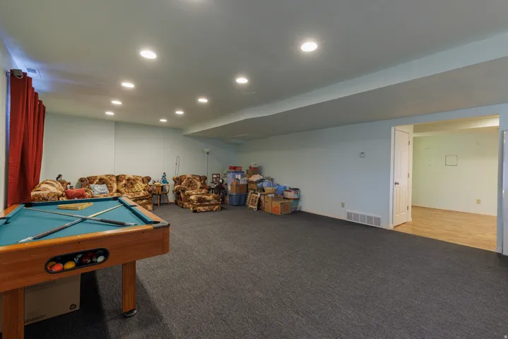 Recessed lighting throughout, wall-to-wall carpeting, and a doorway leading to a room with wood-finish flooring