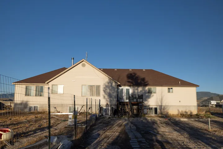 Rear exterior with light-colored siding, a brown shingle roof, and a visible deck with stairs