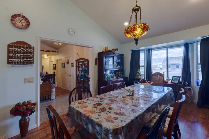Vaulted ceiling, decorative chandelier, bay window, wood-finish flooring, and a wide interior doorway