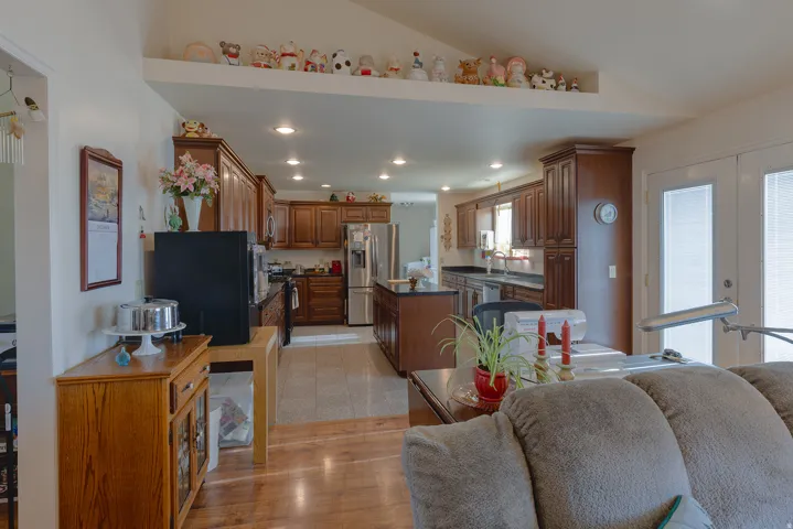 Open-concept living area with wood-finish flooring, vaulted ceiling, recessed lighting, and double glass-paneled doors