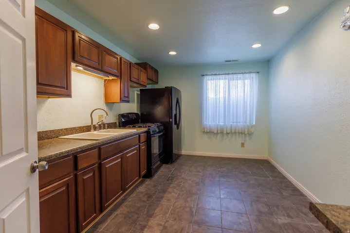 Dark wood cabinetry, tiled flooring, built-in recessed lighting, double basin sink, and a black appliance suite