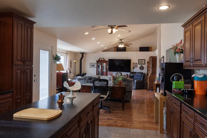 Open-concept living area featuring vaulted ceilings, wood-finish flooring, recessed lighting, and a wood-burning stove