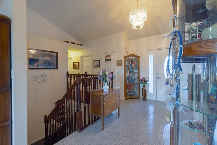 Vaulted ceiling, decorative chandelier, wood-finish staircase with balusters, light-colored flooring, and an entry door with a decorative glass insert