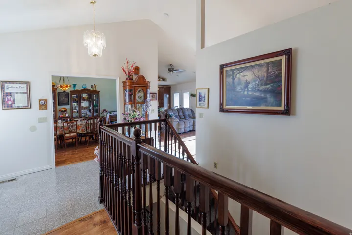 Vaulted ceiling with an ornate chandelier, dark wood-finish banister, and light-toned wall finishes