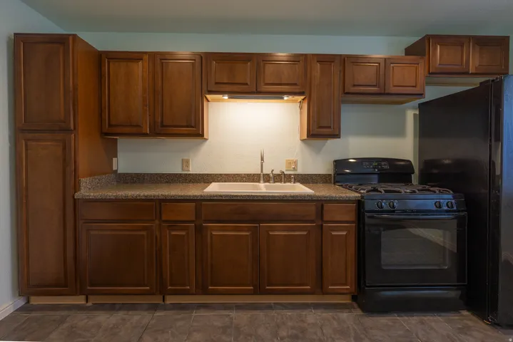 Kitchen featuring wood-finish cabinetry, a double basin sink, under-cabinet lighting, a black gas range, and a black refrigerator
