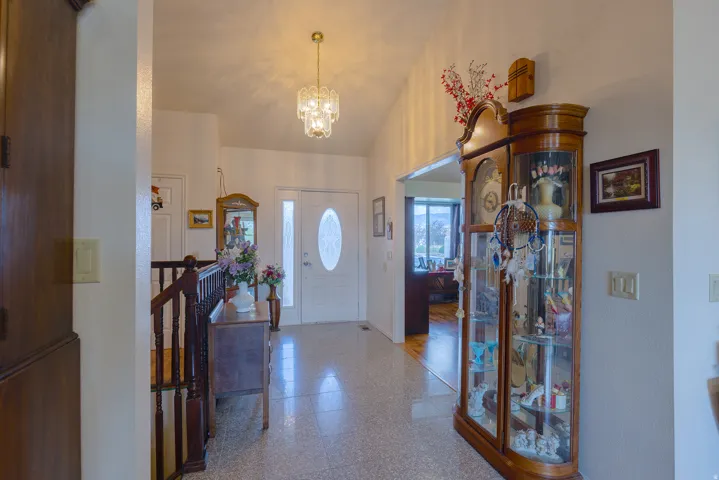Vaulted ceiling entryway featuring a decorative chandelier, white front door with oval glass insert, and terrazzo-style flooring