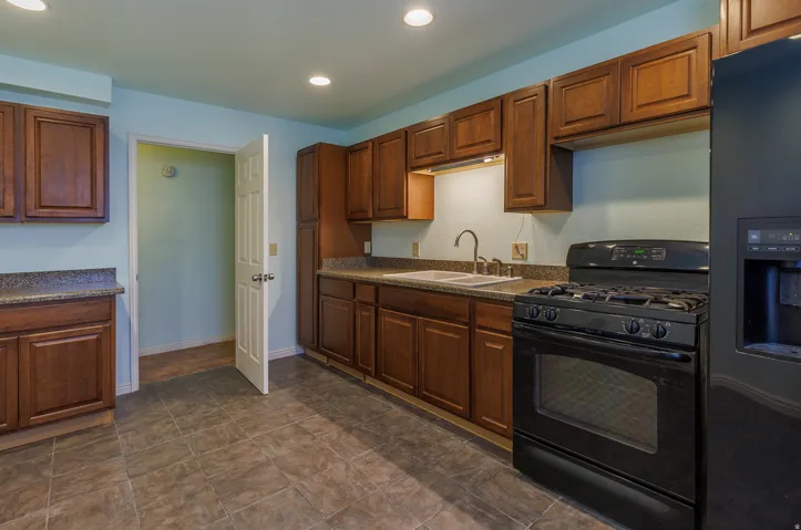 Kitchen featuring wood-finish cabinetry, dark countertops, a black gas range, and a black refrigerator