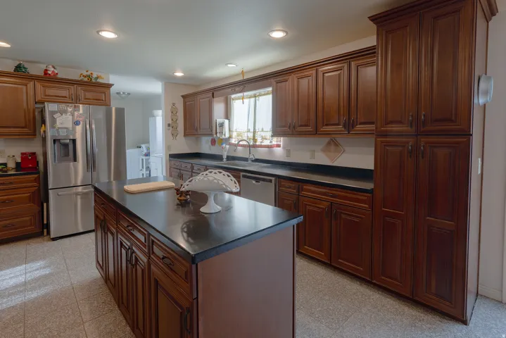 Kitchen featuring abundant wood-finish cabinetry, a central island with a dark countertop, recessed lighting, and tile flooring