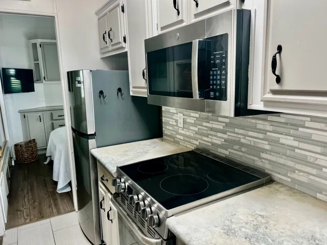 Modern kitchen featuring stainless steel appliances, a built-in microwave, a black electric cooktop, light-colored cabinetry with dark hardware, and a mosaic tile backsplash