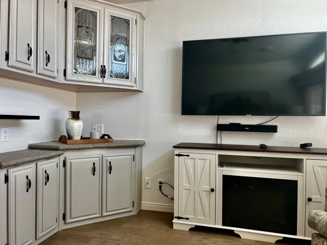 Built-in cabinetry with decorative glass inserts, wood-finish flooring, and a media console with an integrated electric fireplace