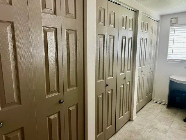 Bi-fold panel doors with black hardware, ceramic tile flooring, and a window with horizontal blinds