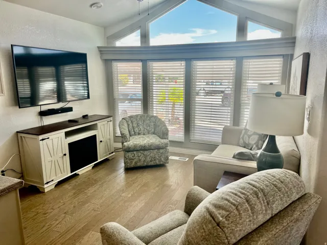 Vaulted ceiling with transom windows, wood-finish flooring, built-in media console, ceiling fan, and window blinds