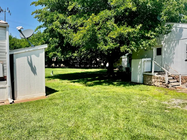 Expansive exterior featuring a large shade tree, manicured lawn, and a dedicated storage shed