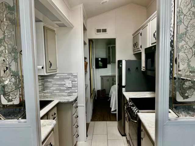 Galley kitchen featuring light-toned cabinetry, a mosaic tile backsplash, black appliances, light-colored countertops, and wood-finish flooring