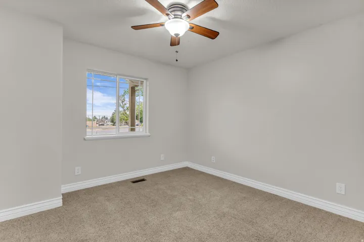 Neutral tone wall paint, carpet flooring, a ceiling fan with light fixture, and a window with white trim