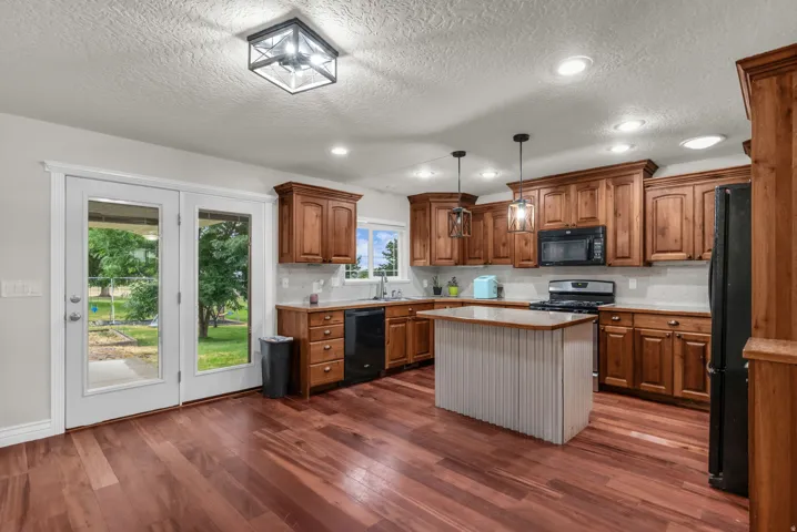 Wood-finish flooring, wood cabinetry, built-in kitchen appliances, central island, and glass-panel double doors