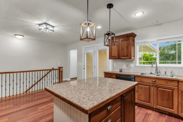 Kitchen featuring wood-finish flooring, an island with a light-toned countertop, wood cabinetry, stainless steel sink, and a white tile backsplash