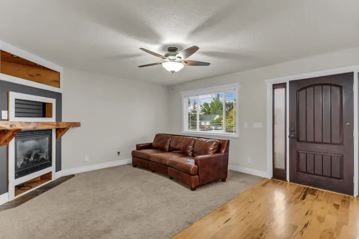 Integrated fireplace with a rustic wood mantel, ceiling fan with integrated lighting, natural wood-finish flooring, and a paneled entry door with sidelight