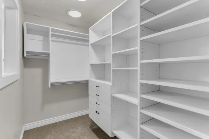 Custom built-in white cabinetry, multiple hanging rods, integrated shelving, pull-out drawers with black hardware, and recessed lighting