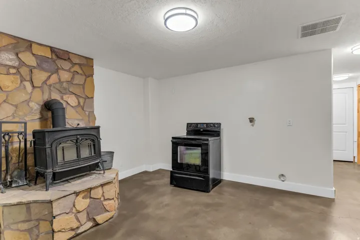 Stone-clad fireplace with a cast iron wood-burning stove, concrete flooring, and recessed lighting